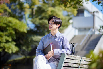 大学キャンパスのベンチに座る日本人大学生の男性