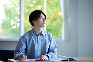 家のリビングで勉強をする日本人大学生の男性 - obrazy, fototapety, plakaty