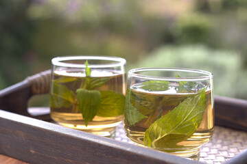 Herbal Mint Tea. Spearmint Tea in a clear glass on a bamboo tray serving with fresh mint leaves and flower in the morning sunrise. Healthy food concept Herbal Tea. 