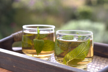 Herbal Mint Tea. Spearmint Tea in a clear glass on a bamboo tray serving with fresh mint leaves and flower in the morning sunrise. Healthy food concept Herbal Tea. 