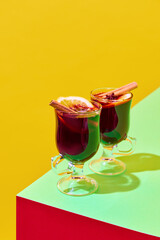 Glasses with delicious red mulled wine with oranges and cinnamon against colorful background. Concept of winter season, Christmas holidays, traditional drinks, taste. Poster