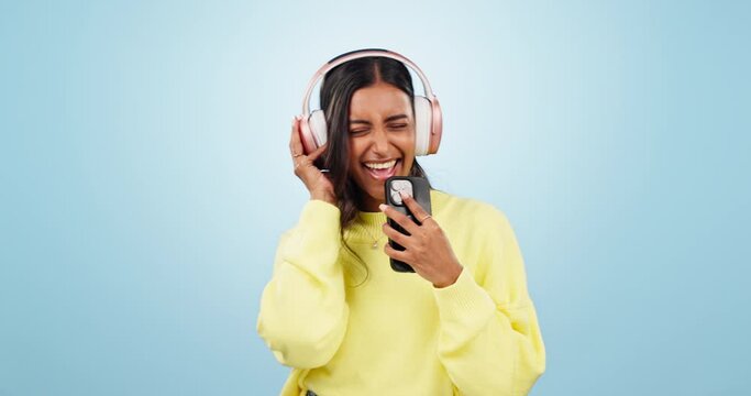 Music, phone or Indian woman in studio singing a song or radio audio on subscription in headphones. Relax, dance or happy girl streaming on an online mobile app isolated on a blue background for joy