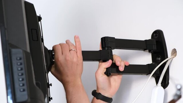 A man rotates a flat-screen TV hanging on a bracket, demonstrating a wide angle of rotation of the screen. The TV bracket demonstration. Mount bracket for LCD monitor, plasma TV, LED display device