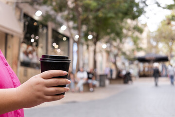 A close-up of a woman holding a black plastic coffee cup in hand. Coffee break in the city center...