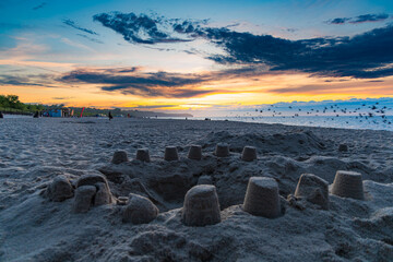 Circle sandcastle in front of beautiful dark golden sunset at golden hour at the beach next to dark...