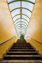 Small tunnel with yellow walls and green arcs and with downstairs to underground passage under streets - obrazy, fototapety, plakaty