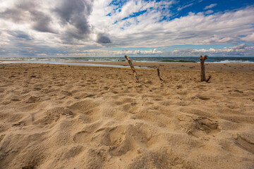 Beautiful landscape of stormy sea seen from big sandy beach full of dunes and with three big stakes...