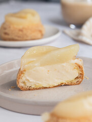 A French cream puff crack bun (Choux au Craquelin) topped with poached pear fruit, cut in a half filled with pear pastry cream filling.  It's a dessert base of savory choux dough bun and cream