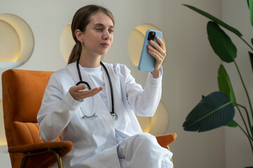 Smiling female doctor talking on the phone with a patient makes a video call to a telemedicine...