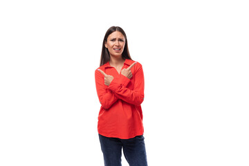 young charming brunette employee woman dressed in a red loose shirt points with her hands to the side of space on a white background