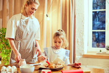 Little girl, child cooking at home with her mother, putting butter on top of prepared croissants. Domestic bakery. Concept of cookie day, motherhood, childhood, holidays, family