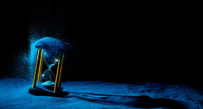 Hourglass is sand of time age, Life pour blue sand into hourglass to add more limited time. Deadline extended time management hope concept hour glass. Black background shadow life clock passing by