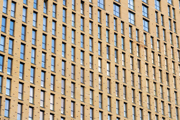Low-angle view of facade of building with brick wall and windows as geometric pattern. Perspective texture view of many windows in row on facade of city apartment building