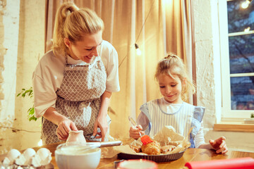 Little girl, child cooking at home with her mother, putting butter on top of prepared croissants. Domestic bakery. Concept of cookie day, motherhood, childhood, holidays, family