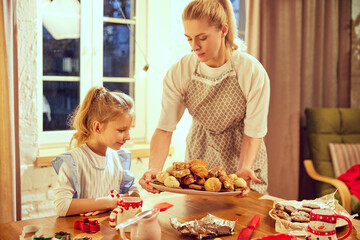 Happy smiling young woman carrying prepared cookies and croissants. Little girl, daughter cooking at home. Coziness. Concept of cookie day, motherhood, childhood, holidays, family