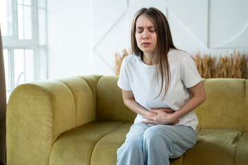 Woman experiences abdominal pain while sitting at home on the couch. 