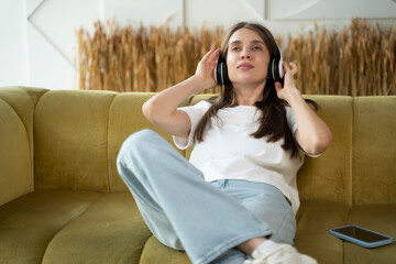 Happy woman listening to music in headphones on sofa at home. 