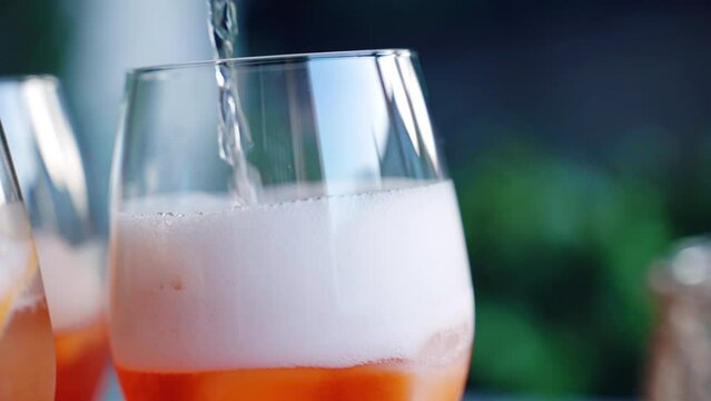 Pouring cool prosecco into the glass with ice cubes, aperol spritz and orange fruit slices, fizzy refreshing cocktail, alcohol summer cocktail drink 