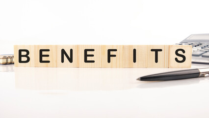BENEFITS word word assembled from wooden cubes next to a calculator, pen and notepad
