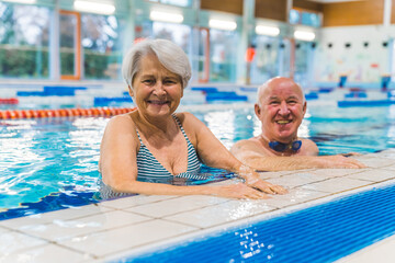 smiling and joyful aged couple at the side of the indoor pool looking at the camera. High quality photo