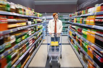 A man stands with a shopping cart in a supermarket between the shelves with drinks