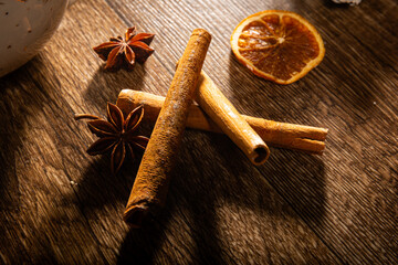 Dried orange, anise and cinnamon on a wooden table with a white mug in the background illuminated by soft rays of light