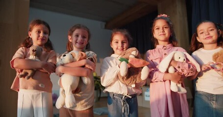 Zoom Out portrait of five preschool age girls with their soft toys standing and looking at the camera and smiling in a club room for preparing children for school