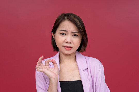 A snobbish young woman making a condescending explanation to someone she looks down on. A mean lady looking repulsed. Studio shot with burgundy background.