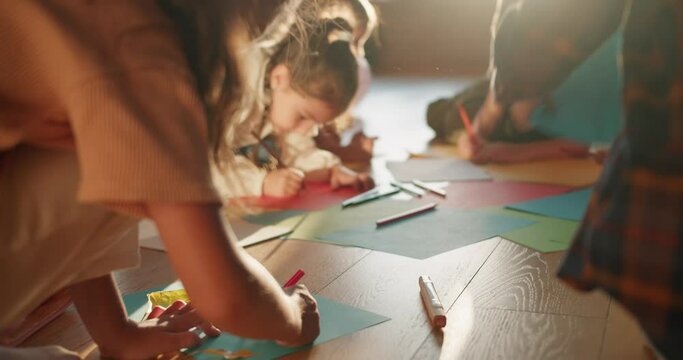 Close-up shooting of preschool children sitting on the floor and drawing on multi-colored paper using pencils in a club for preparing children for school