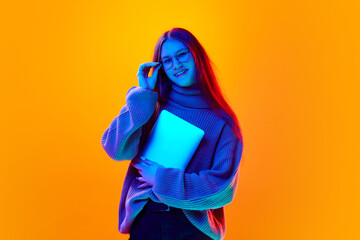 Portrait of cheerful girl, student, freelancer dressed wool sweater holding tablet in neon light...