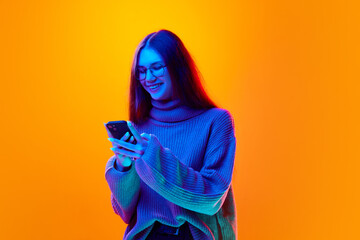 Cheerful young beautiful woman make online order at mobile phone on gradient studio background in neon light, filter. - obrazy, fototapety, plakaty
