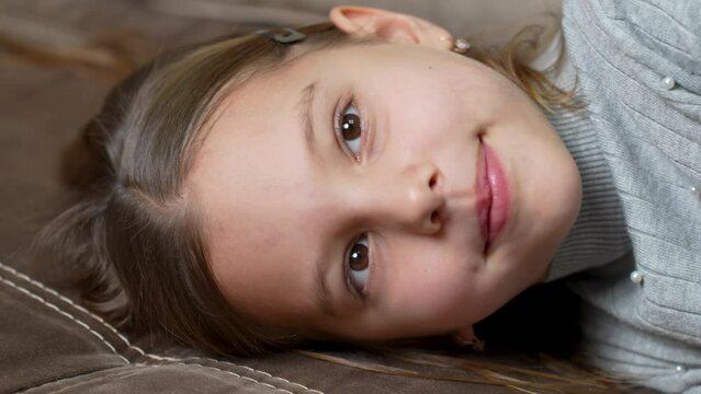 Cute little girl lies on sofa, smiling and looking at camera