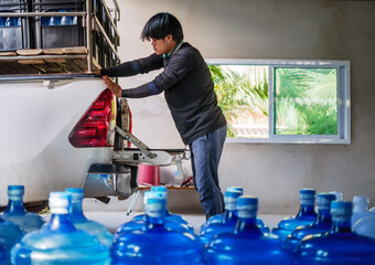 Workers lift drinking water .clear and clean in blue plastic gallon into the back of a transport truck purified drinking water inside the production line to prepare for sale.  small business
