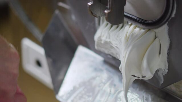 Close shot of man hands with a stirring paddle mixing ice cream from freezer in a steel container. High quality 4k footage