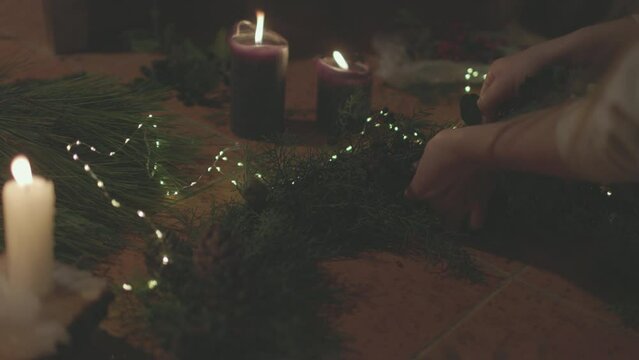 A girl collects New Year's decor. burning candles with Christmas decorations of pine cones around.