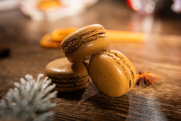 Chocolate macarons on a wooden table among Christmas decorations and snow-covered branches of a...