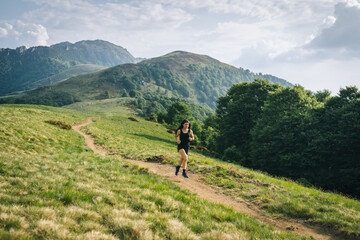 Fototapeta na wymiar Woman trail running through alpine landscape in morning light, view of mountains behind her