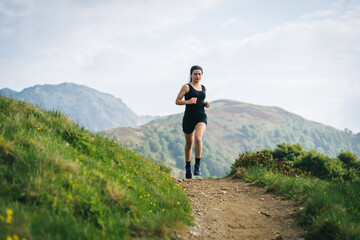 Obraz premium Woman trail running through alpine landscape in morning light, view of mountains behind her