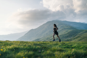 Naklejka na ściany i meble Woman trail running through alpine landscape in morning light, view of mountains behind her