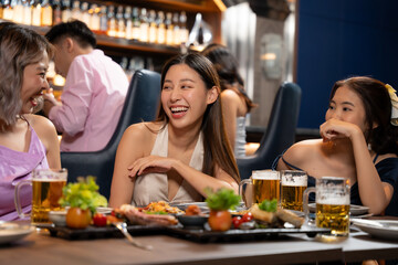 Beautiful Asian woman is Relishing a Delightful Dinner with Friends at a Bar, Immersed in the Joy of a Vibrant Night Party. They Enjoying with Night Party Together. Party and Celebration Concept.