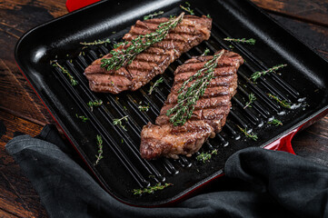 Fried denver beef meat steak with thyme in a grill skillet. Wooden background. Top view