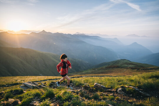 Female trail runner ascending alpine trail in the mountains at sunrise