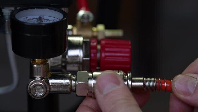 Worker connects orange air hose to air compressor via hose coupling, closeup. Spiral hose for supplying air pressure to the instrument and possibility of working at large distance from the main base