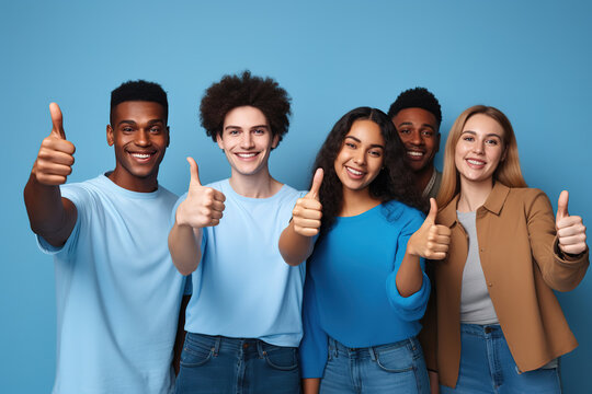 Young people with approving expression looking at camera showing success and like gesture on blue background. Diverse happy multiracial people holding raised thumbs ups.