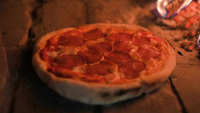 Italian pizza pepperoni is cooked in a wood-fired oven. Pizza with salami in hot oven close up. Food video. UHD 4k video. Slight dolly move