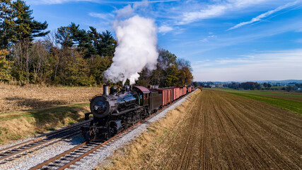 Fototapeta na wymiar An Aerial View of an Antique Steam Freight Passenger Train Blowing Smoke as it Slowly Travels on an Autumn Day