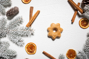 Star-shaped gingerbread on a white snowy background among cinnamon and dried orange and snow-covered branches of a Christmas tree