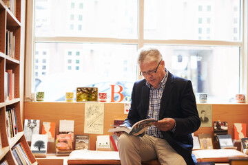 Senior man, library and author reading book for literature, knowledge or story at bookstore. Mature...