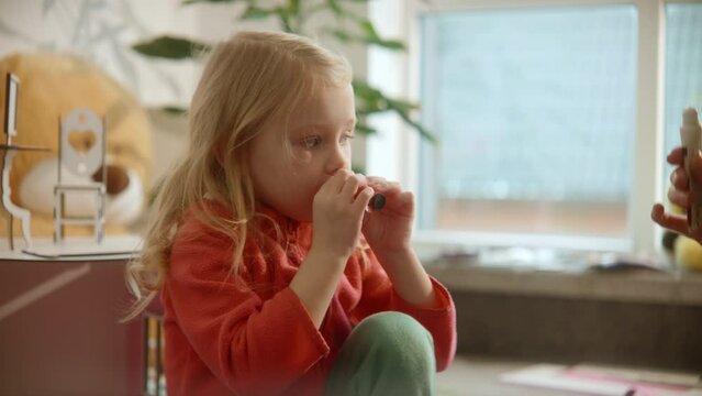 Cute toddler girl learns a process of using lipbalm on her lips, side view, beauty care, girl's growing. Family weekend, female beauty routine, sunny nursery room background. High quality 4k footage
