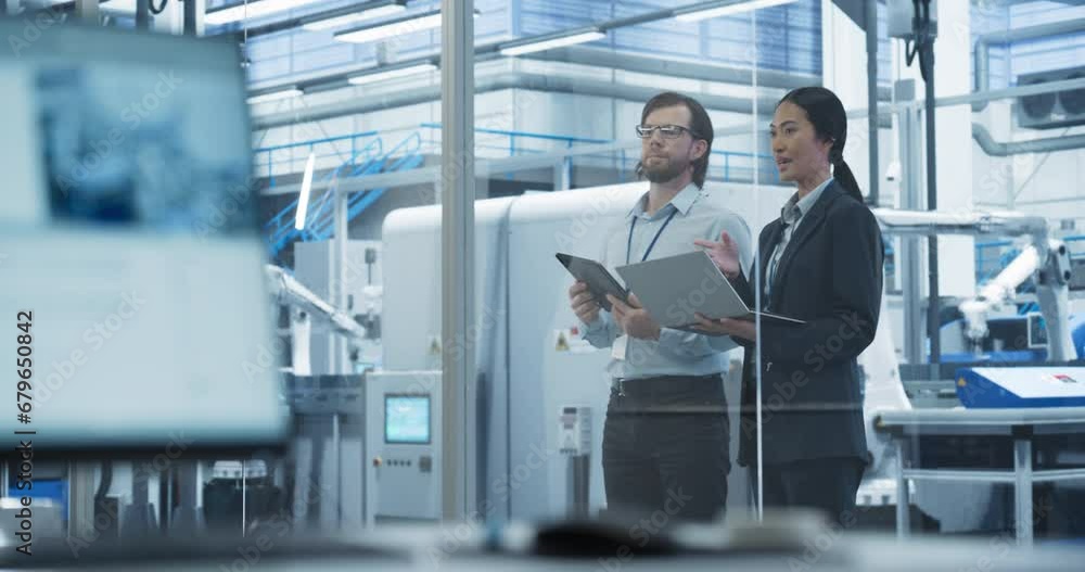 Poster Portrait of a Young Engineer and Happy Asian Project Manager Using Laptop and Tablet Computers, Talking in a Factory Facility with Automated Robots Producing Modern Electronic Components